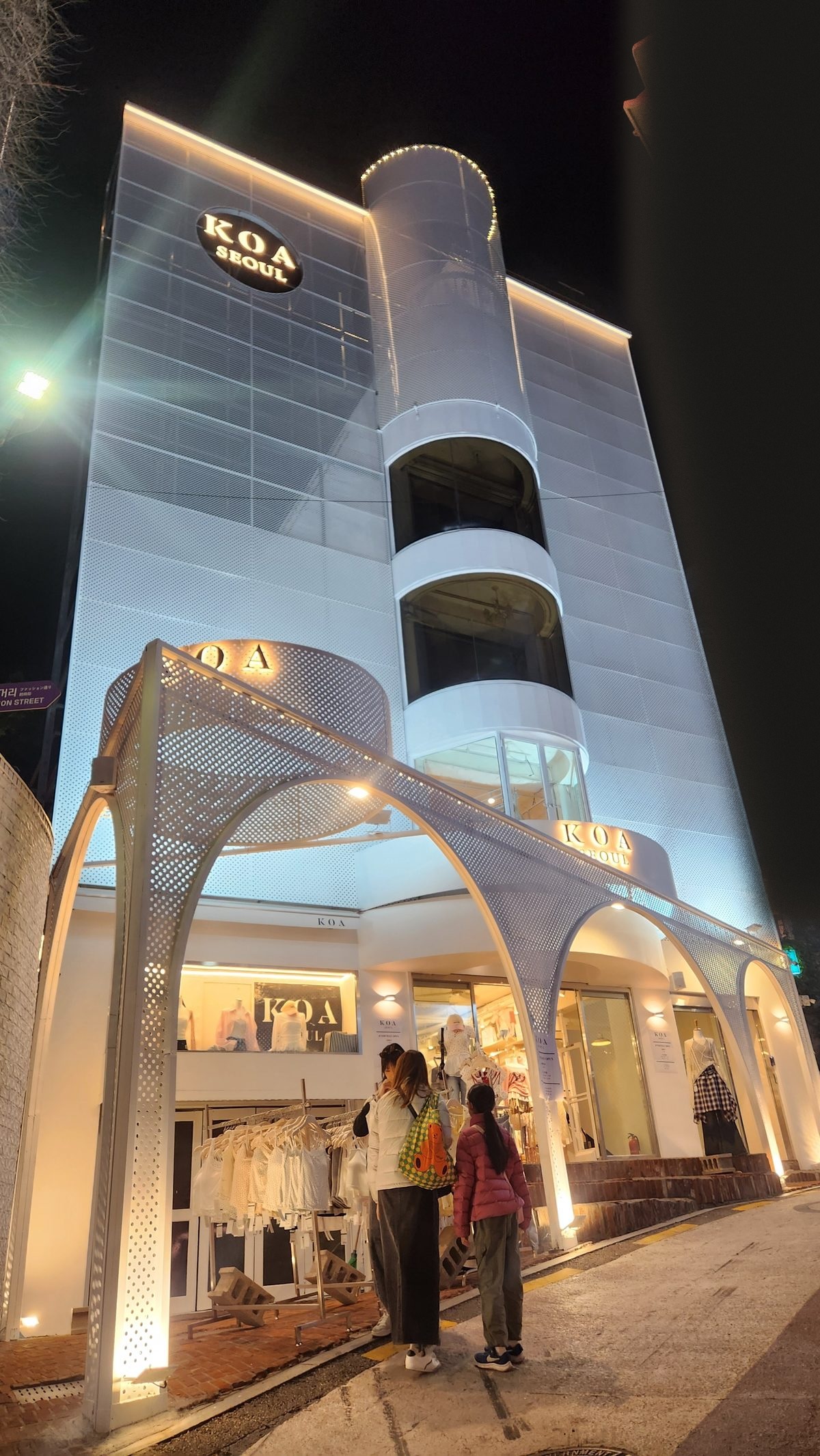 KOA Seoul — a white perforated-metal building lit at night, arches over the entrance
